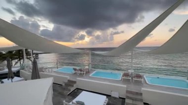 Karayipler 'de lüks bir tatil köyünün balkonundan gün batımının inanılmaz zamanlaması, kristal berrak turkuaz deniz arka planı, jakuzi ve özel havuzlarla donatılmış otel dinlenmek için ideal..