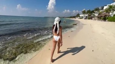 Riviera Maya 'da beyaz kumlu bir plajın keyfini çıkaran seksi genç bir kadın kristal berrak turkuaz Karayip suyunun üzerinde yürüyüp Meksika' daki tatil yerine gidiyor..