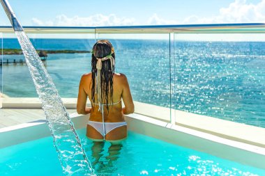 Young tourist woman enjoying the wonderful horizon of the Caribbean Sea, under a shining sun that reflects the crystal clear turquoise blue water that characterizes this ocean. clipart