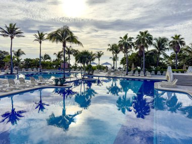 Palm trees and lush green vegetation in a tropical environment reflected in a huge pool at sunrise in the Caribbean, ideal for summer vacations and relaxation. clipart