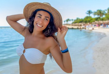 Beyaz bikini giyen bir kadın, el değmemiş bir Karayip plajında güneşleniyor. Onun mutluluk ifadesi, tropikal bir cennetin pitoresk zemininde gençleşme arayışının özüdür..