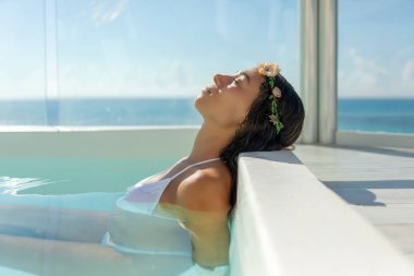 Beautiful young woman in a sexy bikini relaxing in a jacuzzy under the warm rays of the Caribbean sun, an ideal tropical setting to enjoy a vacation. clipart