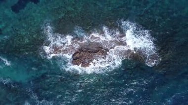 Kayalık bir resife çarpan okyanus dalgalarının yukarıdan aşağıya hava görüntüsü berrak turkuaz ve derin mavi deniz içinde köpüklü beyaz su desenleri oluşturur..