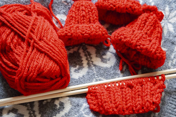 Незавершенный вязальный проект, выполненный из красной пряжи, установленный на сером фоне, с маленькими шляпами эльфов в процессе. Сцена захватывает уютную, праздничную атмосферу, идеально подходящую для показа праздничных сумасшедших.