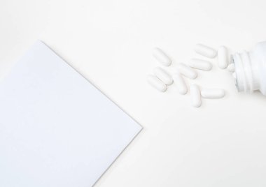 Beyaz haplar ve bir not. Beyaz haplar şişeden dökülüyor, köşede beyaz bir kağıt, yazı için yer, estetik beyaz arka plan