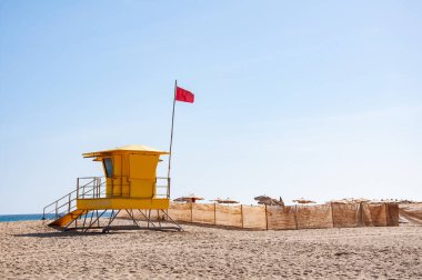 Fuerteventura İspanya 'da kırmızı bayrak taşıyan cankurtaran kulübesi. Bulutsuz gökyüzü, geniş sahil, okyanus, kıyı şeridi ve yaz