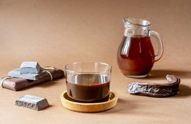 Keçiboynuzu ürünleri - pekmez ve içecek, açık kahverengi arka planda çikolata ve keçiboynuzu kabukları ve metin için boşluk. Keçiboynuzu her zamanki çikolataya göre sağlıklı ve lezzetli.