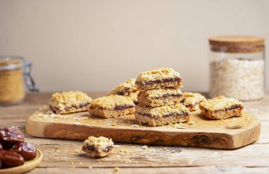 Ev yapımı eski moda yulaf ezmesi ve hurma kareleri ya da ahşap kesim tahtasındaki evlilik barları ve malzemeli kırsal ahşap masa. 