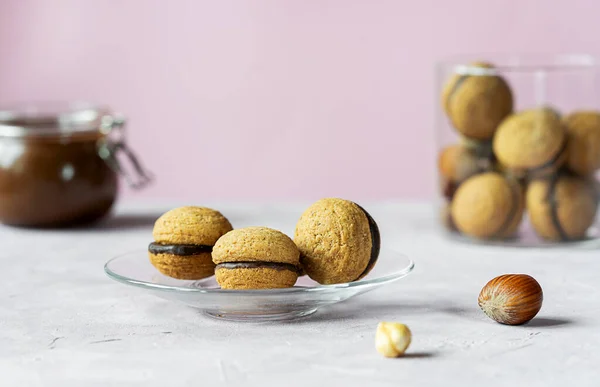 Hazelnut biscuits baci di dama or ladys kisses are traditional Italian dessert made as a sandwich with two cookies and chocolate cream. There are group of cookies on glass plate, jars with chocolate