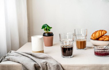 Spring cozy breakfast concept. Two glasses with coffee and milk, croissants, spring plant, jam, linen napkin. Kinfolk style. Copy space for text