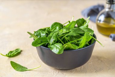 Siyah kasede taze ıspanak, zeytinyağı ve açık kumlu arka planda gri peçete. Yüksek kalite fotoğraf