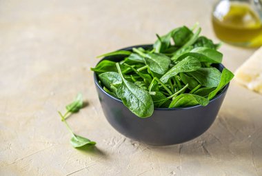 Siyah kasede taze ıspanak, zeytinyağı, sert peynir ve açık kumlu arka planda yeşil peçete. Üst görünüm, kapat, boşluğu kopyala