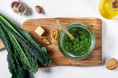 Ev yapımı lahana pesto sosu cam bir kasede servis edilir. Tahtanın üzerinde temel malzemelerle birlikte tahta kesilir. Lahana yaprağı, ceviz, parmesan, sarımsak ve zeytinyağı.