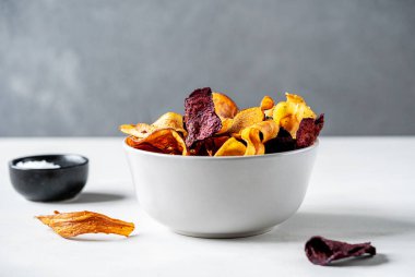 Gri bir kasede sağlıklı renkli sebze cipsleri, açık yüzey üzerinde gri beton arka plan ile deniz tuzu. Vejetaryen yemeği. Sağlıklı yemek kavramı