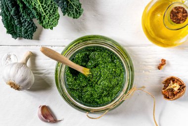 Ev yapımı lahana pesto sosu beyaz ahşap yüzeyde servis edilir. İçinde temel malzemeler vardır. Lahana yaprağı, ceviz, parmesan, sarımsak ve zeytinyağı.