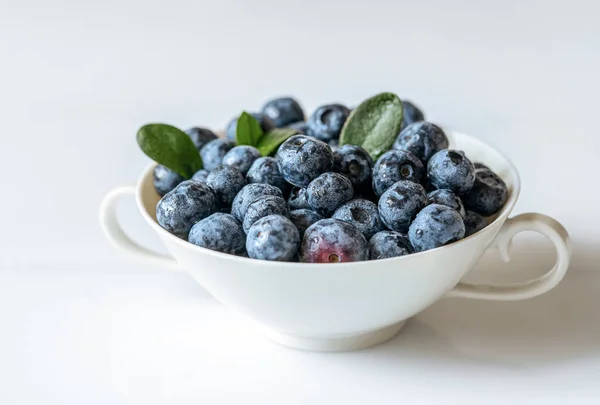 stock image Fresh blueberries in an elegant white teacup on the white background, closeup, top view. Healthy snack concept