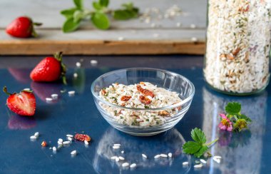 Çilek ve bitkilerle karışık risotto, cam bir kase ve şişe, taze çilek, cam üzerinde adaçayı yaprakları koyu mavi arka plan
