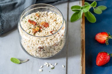 Çilek ve otlarla karışık risotto, cam bir kapta taze çilek, adaçayı, gri ahşap ve mavi arka planda peçete.