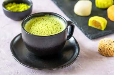 Bir fincan köpüklü kibrit çayı, sade siyah bir fincanda servis edilir, mochi ve kibrit tozu seçimi arka planda yavaşça bulanıklaşır..