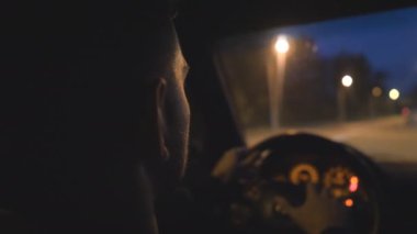 Genç adam direksiyonda el ele tutuşuyor ve akşamları modern bir otomobil kullanıyor. Adam gece vakti otoyolda araba sürüyor. Erkek sürücü boş yolda SUV arabasıyla hareket ediyor. Yavaş çekim.