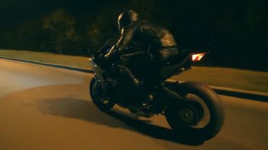 Motosikletli, gece yolunda motosikletiyle yarışıyor. Miğferli genç adam akşam caddesinde modern spor motosikletle hızlı gidiyor. Alacakaranlıkta bisiklet süren adam. Özgürlük ve macera kavramı. Yan görünüm.