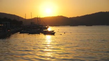 Deniz yüzeyinde yüzen balıkçı teknelerinin güzel manzarası ve arka planda günbatımı. Deniz kıyısının yakınında duran balıkçı gemileri. Altın güneş ışığı okyanus ortamını aydınlatıyor. Manzaralı deniz manzarası.