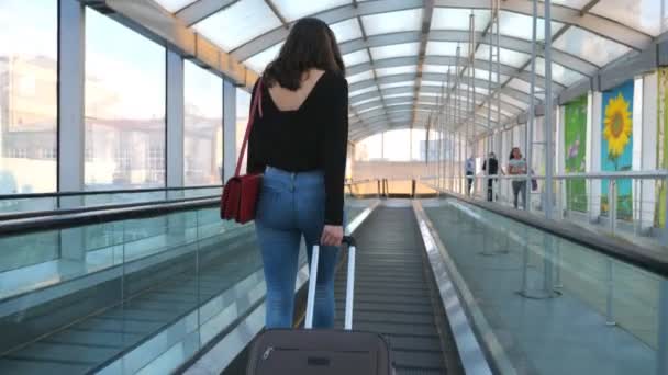 一个无法辨认的年轻姑娘背着她的行李在自动扶梯上走着 性感女人的腿带着轮子去拉手提箱 女士要去旅行 旅行或度假的概念 慢动作回视 — 图库视频影像
