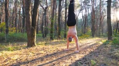 Kaslı bir adam, gün batımının arka planında ormanda amuda kalkıyor. Manzaralı ortamda güçlü jimnastik eğitimi. Sporcu dışarıda gösteri yapıyor. Aktif yaşam tarzı kavramı. Dolly vurdu..