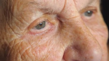 Portrait of elderly woman watching pensive to something. Close up of female eyes with wrinkles around. Grandmother looking calmly into distance and thinking. Slow motion Detail view.