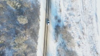 Kış günü ormanın güzel kırsal kesiminde SUV sürüyordu. Karla kaplı buzlu yolda uçan beyaz arabanın görüntüsü. Otomotiv üzerinde uçmak manzaralı bir yolda ilerlemek. Üst görünüm.