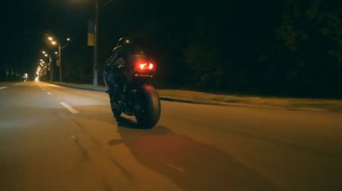 Night City caddesinde, modern motorsikletle hızlı giden bir adam. Motosikletli, boş yolda motosikletiyle yarışıyor. Alacakaranlıkta bisiklet süren adam. Özgürlük ve macera kavramı. Düşük açı. Yakın plan.