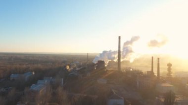 Endüstri bölgesinin hava görüntüleri borulardan atmosfere duman yayıyor. İHA fabrikanın üzerinde uçuyor ya da bitki zehirli buharı arka planda güneş ışığıyla havaya yayıyor. Doğa kirliliği sorunu. Üst görünüm.