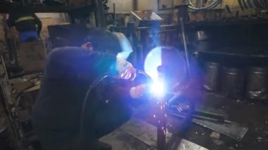 Endüstriyel üretimde koruyucu maske kaynak işçisi. Adam metal parçalarını birbirine kaynaştırıyor. Kaynakçı iki çelik detay arasında ortaklık yapıyor. Atölyede el emeği.