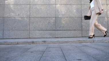 Unrecognizable business woman walking near modern building. Confident businesswoman in suit going on city street to meeting in office. Successful lady in formal wear commuting to work. Slow motion.