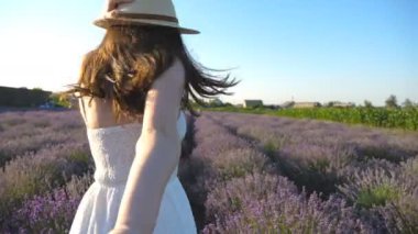Şapkalı gülümseyen kadın koşuyor ve kameraya bakıyor. Lavanta tarlasında koşarken erkek elini tutan mutlu kız. Mutlu çift çiçek çayırında eğleniyor. POV Yavaş çekim.