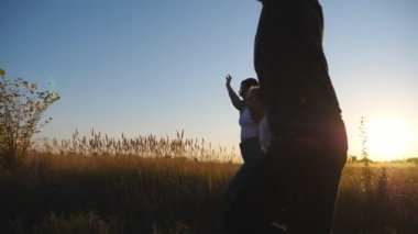 Anne ve baba ve küçük kızı gün batımında kırsal alanda gökkuşağı uçurtmalarıyla koşuyorlar. Genç ebeveynler ve küçük tatlı kız el ele tutuşup çimen tarlasının yakınındaki yolda koşuyorlar. Dolly vurdu..