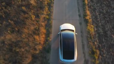 Yaz akşamında şehir yolunda uçan elektrikli arabanın görüntüsü. Kırsal kesimden geçen modern bir araç. Çevre dostu araba otoyol boyunca elektrik yükü ile gidiyor. Üst görünüm.