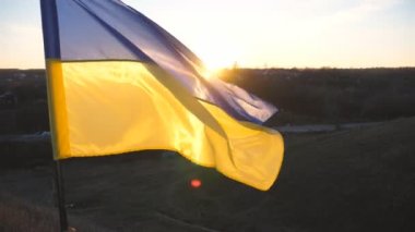 Ukrayna bayrağı gün batımına karşı rüzgarda dalgalanıyor. Ukrayna 'nın sarı-mavi ulusal sembolü. Rus saldırısına karşı barış ve destek kavramı. İstila direnişi ve savaşta zafer.