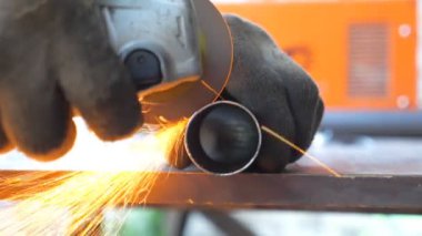 Metal işlemede dairesel testere ile detaylı görüş. Makinistin elleri enstrüman tutuyor ve metali öğütüyor. Garajda ya da atölyede demir kesen bir işçi. Parlak kıvılcımlar uçuşuyor. Kapat..