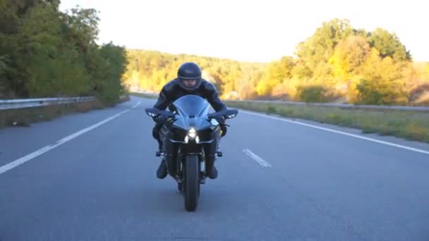 秋の高速道路でバイクに乗ってヘルメットに身を包んだ男 オートバイ愛好家はヘッドライトをつけた田舎道でバイクを運転している 自由と旅行の概念 スローモーションフロントビューを閉じる — ストック動画