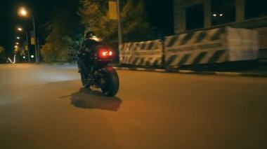 Şehrin gece caddesinde modern motosiklet süren bir adam. Motosikletli, akşam saatlerinde motosikletiyle yarışıyor. Yolculuk sırasında bisiklet süren adam. Özgürlük ve macera kavramı. Arka plan Kapat.