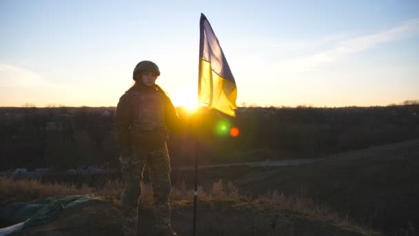 軍の制服を着た女性は日没に対して立ち上がり ウクライナの国旗を掲揚した 女性のウクライナ軍兵士の旗を振って保持 ロシアの侵略に対する勝利 侵入抵抗概念 — ストック動画