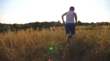 Genç çocuk güneşli günde yeşil çim alan, çalışan için takip. Çim açık koşu çocuk. Mutlu erkek çocuk yaz çayır üzerinde doğada eğleniyor. Ağır çekim arka geri görüntülemek.