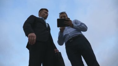 İki genç işadamları bahsediyoruz ve kullanarak tablet pc açık. İş erkek dışında dijital tablet ile gökyüzü arka plan üzerinde çalışıyor. Mobil teknoloji uygulayarak iş arkadaşları. Düşük görüş yavaş hareket açısı.