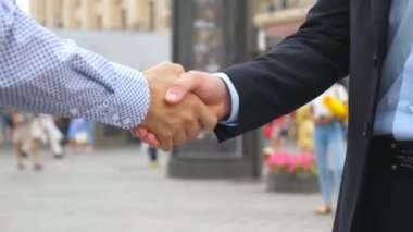 Kentsel ortamda birbirlerini tebrik iki iş adamları. İş karşılıklı açık. Erkek silah sallayarak. İş arkadaşları karşılamak ve şehir arka planda el sıkışın. Yavaş hareket kapatmak.