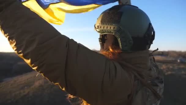 乌克兰军队中的女兵挥舞着乌克兰国旗 身穿军服 头戴安全帽的女孩升起了黄蓝色的旗帜 战胜俄国侵略的胜利抗入侵的概念 — 图库视频影像