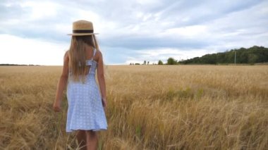 Bulutlu bir günde buğday tarlasında yürüyen uzun sarı saçlı şirin çocuğu takip edin. Hasır şapkalı küçük kız arpa otlağının üzerinden geçiyor. Elbiseli küçük çocuk altın tarlasında vakit geçiriyor..