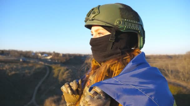 乌克兰女兵站在乌克兰国旗下 遥望远方 身穿军服 头戴安全帽的女人满怀希望地看着地平线 战胜俄罗斯的侵略 — 图库视频影像