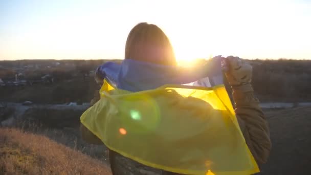 拿着乌克兰国旗的乌克兰女兵 身着军服的女孩在蓝天的映衬下升起了黄蓝色的旗帜 战胜俄国的侵略和战争的结束 靠近点 — 图库视频影像