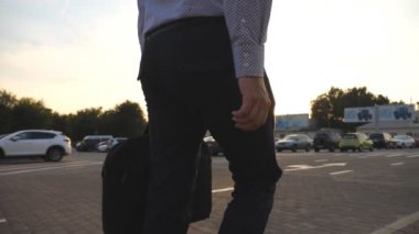 Sunrice saatinde otoparkta yürüyen evrak çantalı genç bir işadamı. İşe gidip gelen bir iş adamı. Kendine güveni tam bir adam sabah ofisine gidiyor. Yavaş çekim. Yakın çekim..